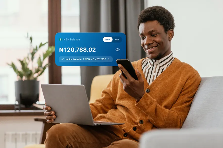 A freelancer checking his NGN balance on his phone while working on a laptop